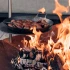 Höfats TRIPLE 120 Bålfad i Corten stål med brændende træstammer, placeret på en hvid overflade. Bålfadet har et moderne design o