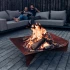 Höfats TRIPLE 120 Bålfad i Corten stål med brændende træstammer, placeret på en hvid overflade. Bålfadet har et moderne design o