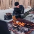 Höfats TRIPLE 120 Bålfad i Corten stål med brændende træstammer, placeret på en hvid overflade. Bålfadet har et moderne design o